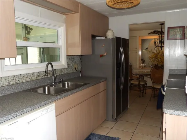Kitchen featuring light cabinets, dishwasher, stainless steel refrigerator with ice dispenser, range with electric stovetop, and light tile patterned floors