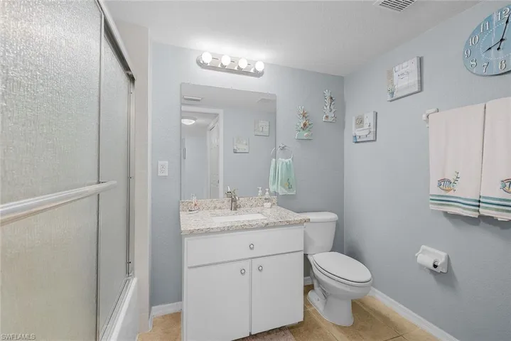 Full bathroom with vanity, light tile patterned floors, and a textured wall