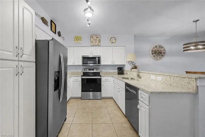 Kitchen with appliances with stainless steel finishes, light stone countertops, light tile patterned floors, white cabinets, and a peninsula