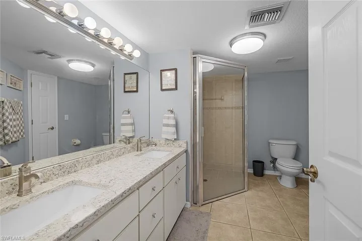 Full bath featuring double vanity, light tile patterned flooring, and a stall shower