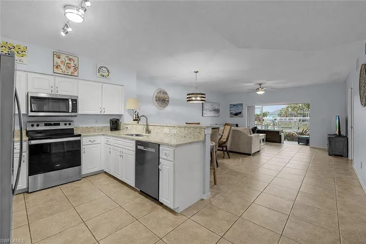Kitchen featuring stainless steel appliances, white cabinets, light stone countertops, a peninsula, and open floor plan