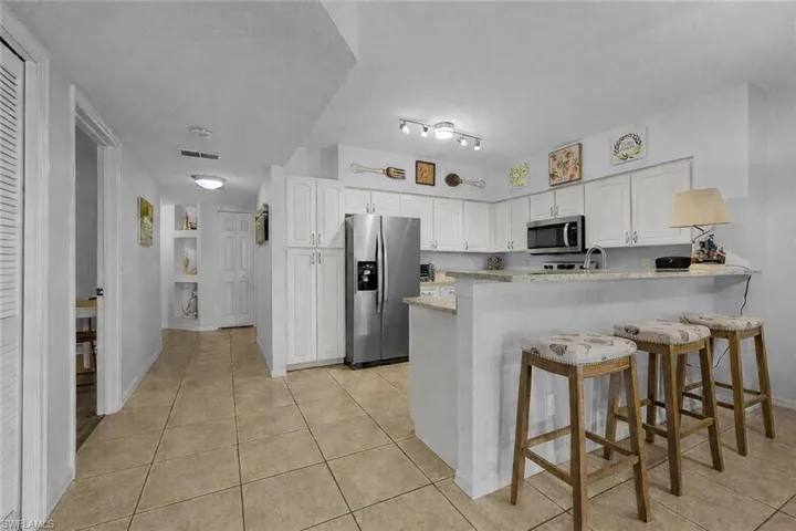 Kitchen with a peninsula, white cabinetry, stainless steel appliances, a breakfast bar area, and light tile patterned floors