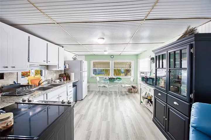 Kitchen featuring a sink, range, white cabinetry, freestanding refrigerator, and light wood-type flooring