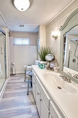 Bathroom featuring a shower stall, vanity, wood finished floors, a textured ceiling, and wainscoting