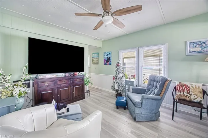 Living room with ceiling fan, light wood-style flooring, and a decorative wall
