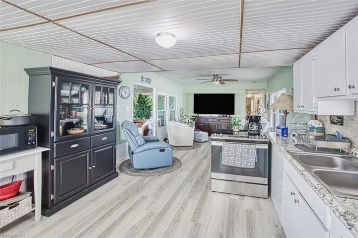 Kitchen featuring electric stove, a sink, black microwave, ceiling fan, and light wood-style flooring