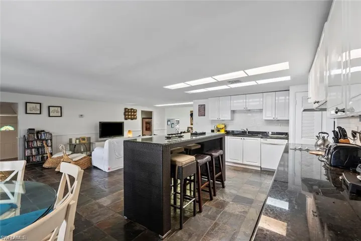 Kitchen with white cabinetry, a breakfast bar, dark stone finish floors, a kitchen island, and white dishwasher