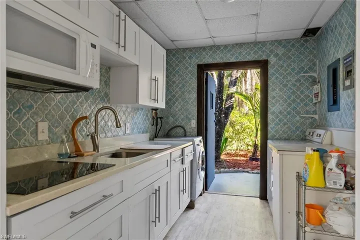 Kitchen featuring a drop ceiling, white microwave, black electric stovetop, washer / clothes dryer, and white cabinetry