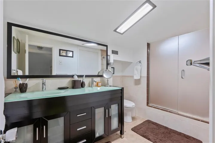 Full bathroom with double vanity, tile walls, a wainscoted wall, light tile patterned flooring, and a shower with door