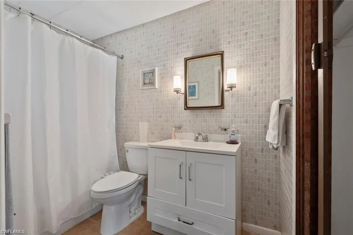 Full bath with a shower with curtain, vanity, tile walls, and light tile patterned floors