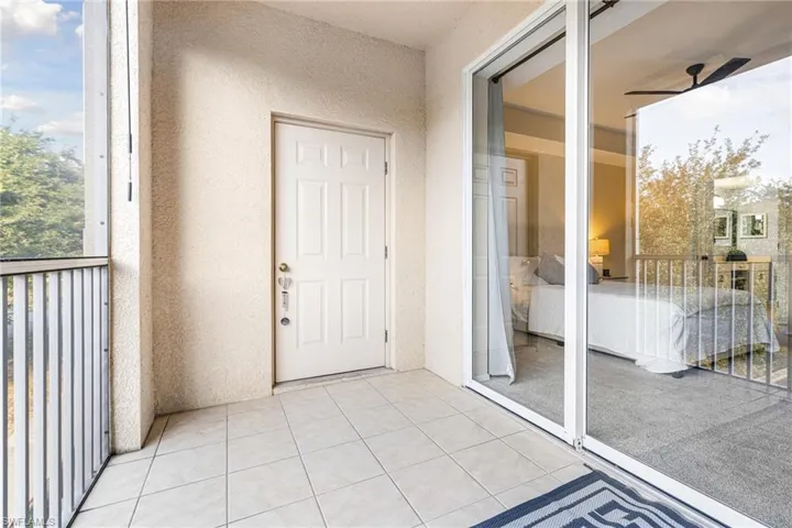 Tiled balcony with a white paneled door, sliding glass doors, and a metal railing