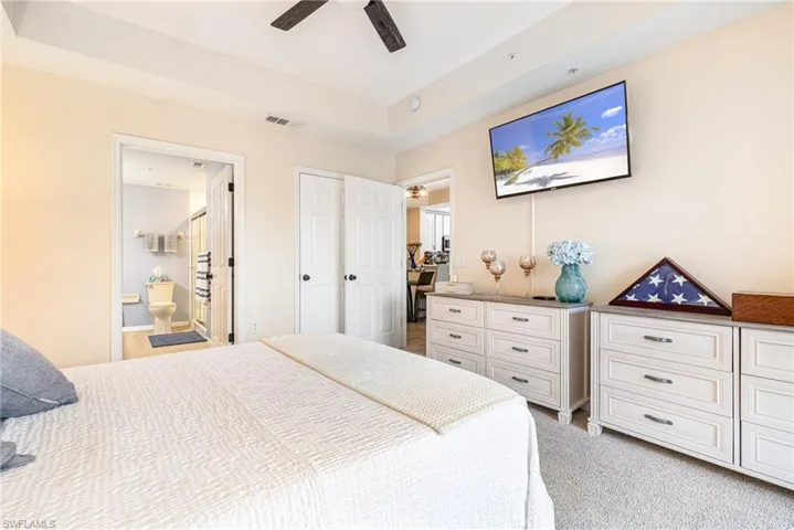 Carpeted bedroom featuring a tray ceiling, ceiling fan, and direct access to a full bathroom