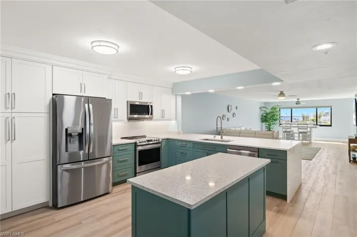 Kitchen with green cabinets, a peninsula, white cabinets, stainless steel appliances, and a sink