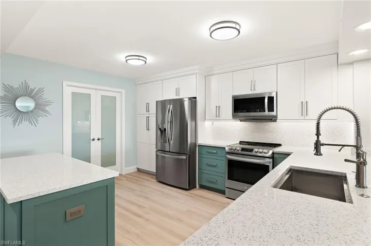Kitchen featuring a sink, stainless steel appliances, green cabinetry, and white cabinets