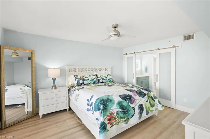 Bedroom with baseboards, visible vents, light wood finished floors, ceiling fan, and ensuite bathroom