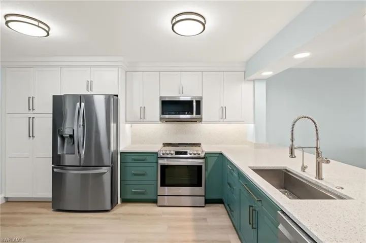 Kitchen featuring green cabinetry, light wood-style floors, white cabinets, stainless steel appliances, and a sink