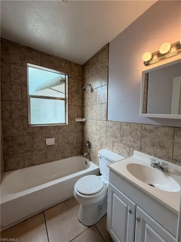 Full bath with tile walls, vanity, washtub / shower combination, light tile patterned flooring, and wainscoting