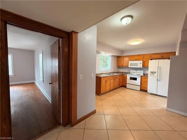 Kitchen with white appliances, wood finish cabinetry, light tile patterned floors, and light countertops