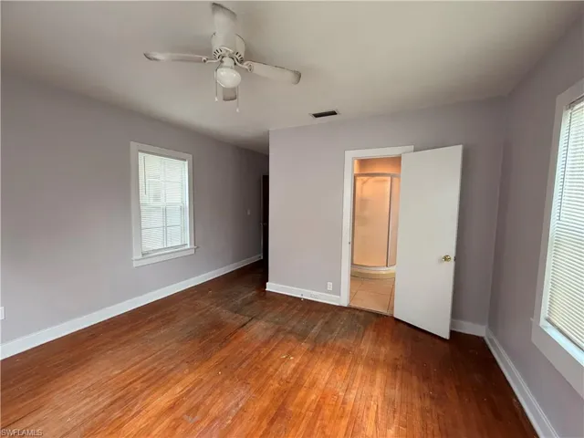 Unfurnished bedroom with dark wood-style flooring, ceiling fan, and connected bathroom