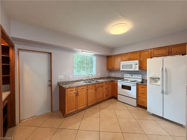 Kitchen featuring white appliances, wood finish cabinets, light tile patterned floors, and dark stone counters