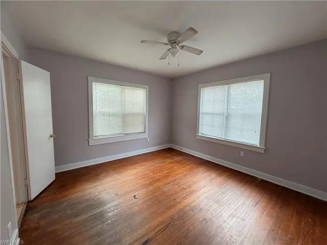 Unfurnished room with dark wood-type flooring, a ceiling fan, and healthy amount of natural light