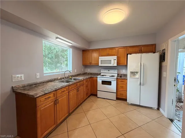 Kitchen with wood finish cabinets, dark countertops, white appliances, and light tile patterned floors