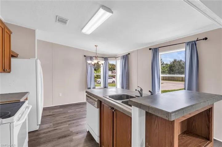 Kitchen with a kitchen island with sink, white appliances, a chandelier, decorative light fixtures, and dark hardwood / wood-style floors