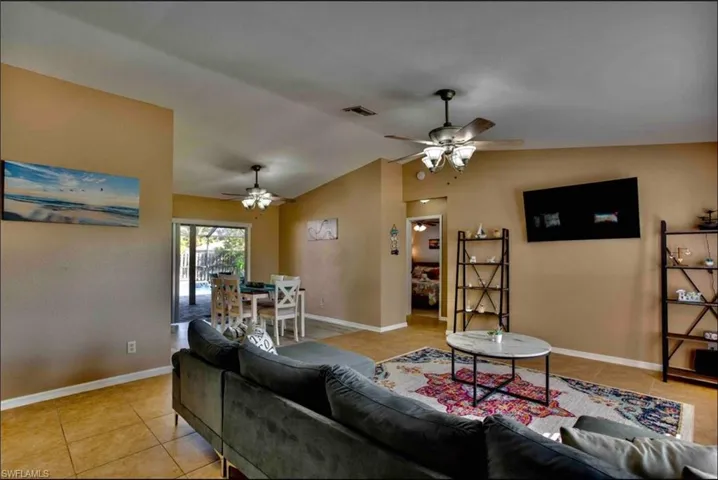 Living area with ceiling fan, light tile patterned floors, vaulted ceiling, and baseboards