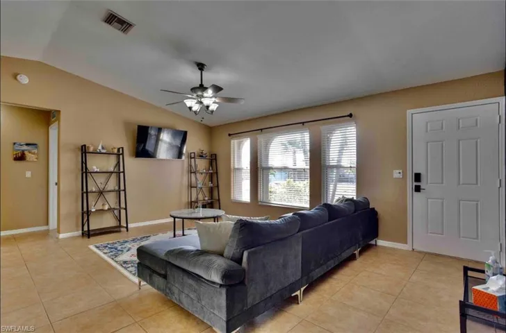 Living area with lofted ceiling, ceiling fan, light tile patterned floors, and baseboards