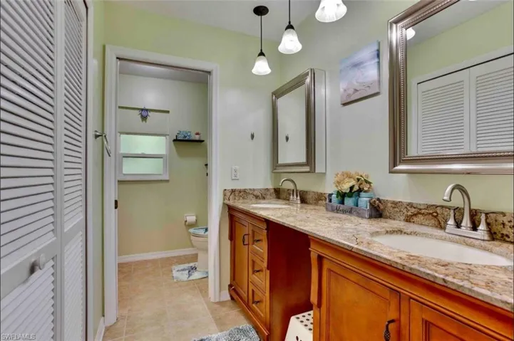 Bathroom with a closet, toilet, double vanity, tile patterned flooring, and baseboards
