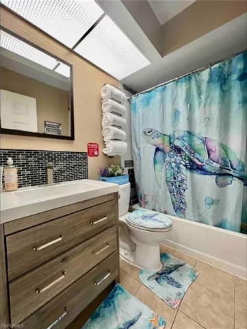 Bathroom with tile patterned flooring, vanity, shower / bathtub combination with curtain, toilet, and decorative backsplash