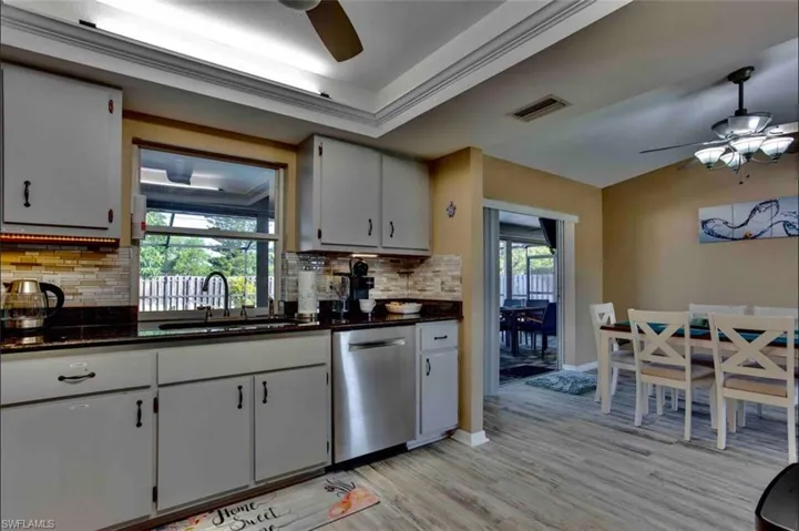 Kitchen with ceiling fan, stainless steel dishwasher, a sink, light wood-style flooring, and decorative backsplash