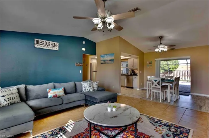 Living area with ceiling fan, vaulted ceiling, light tile patterned floors, and baseboards