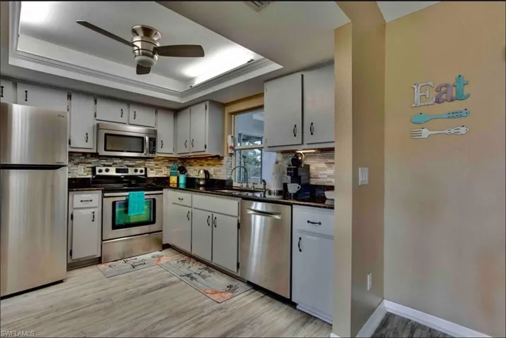 Kitchen featuring appliances with stainless steel finishes, dark countertops, light wood-style flooring, and a tray ceiling