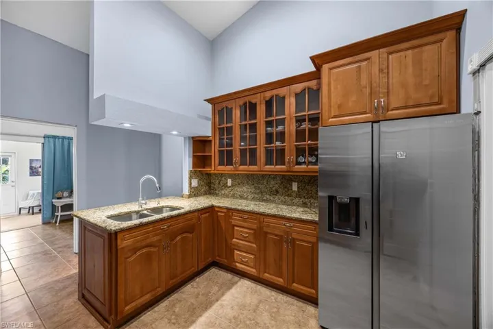 Kitchen with stainless steel fridge with ice dispenser, glass fronted cabinets, light stone countertops, tasteful backsplash, and wood finish cabinets
