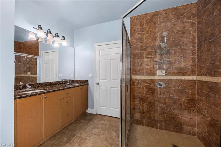 Full bath with double vanity, a shower stall, and dark tile patterned flooring