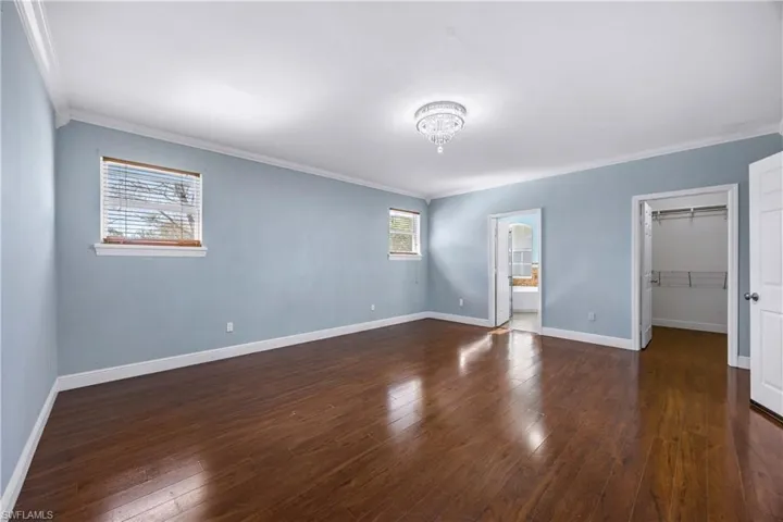 Unfurnished bedroom featuring a spacious closet, dark wood-type flooring, crown molding, and ensuite bath