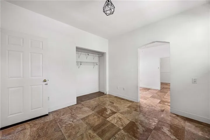 Unfurnished bedroom with arched walkways, a closet, vaulted ceiling, and stone finish floors