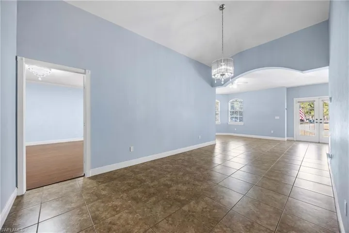 Unfurnished room with suspended lighting, dark tile patterned flooring, french doors, and vaulted ceiling