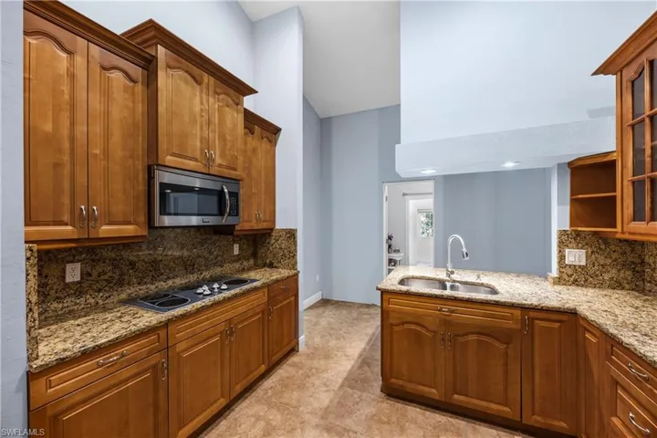 Kitchen with tasteful backsplash, light stone counters, wood finish cabinets, and a peninsula