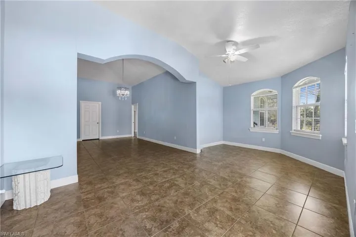 Empty room featuring a ceiling fan, a chandelier, lofted ceiling, dark tile patterned floors, and arched walkways