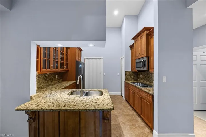 Kitchen with light stone countertops, backsplash, a peninsula, wood finish cabinets, and glass fronted cabinets