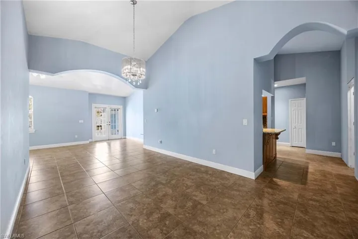 Spare room with arched walkways, vaulted ceiling, dark tile patterned flooring, french doors, and suspended lighting