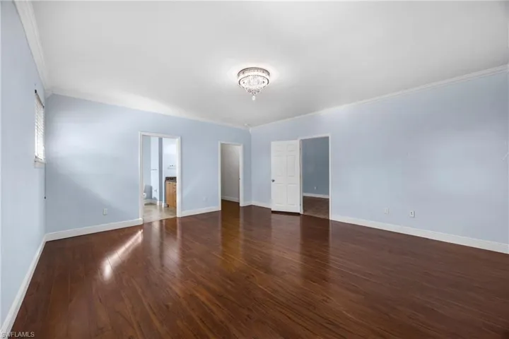 Unfurnished bedroom featuring dark wood-type flooring, ornamental molding, and ensuite bath