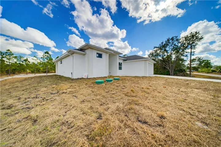 Rear view of property with stucco siding, an attached garage, a lawn, and concrete driveway