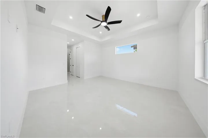 Empty room with a raised ceiling, ceiling fan, and recessed lighting