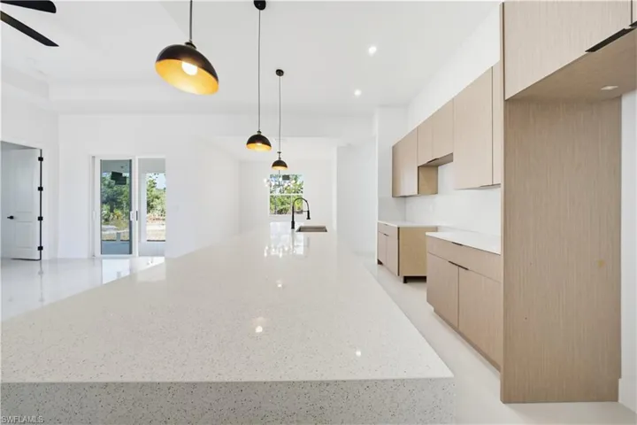 Kitchen featuring modern cabinets, light stone countertops, decorative light fixtures, light brown cabinets, and recessed lighting
