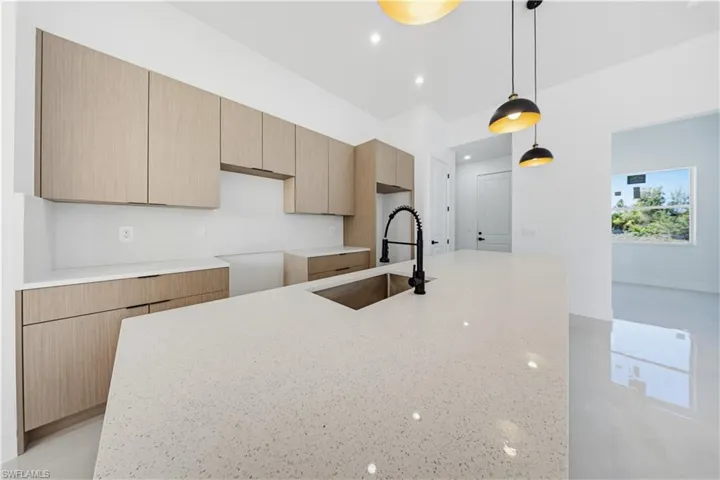 Kitchen with light stone counters, modern cabinets, a kitchen island with sink, hanging light fixtures, and light brown cabinets