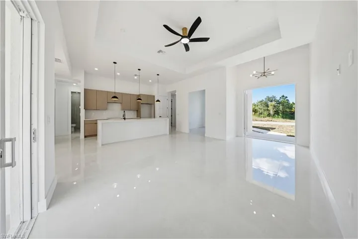 Unfurnished living room featuring a tray ceiling, ceiling fan, and a chandelier