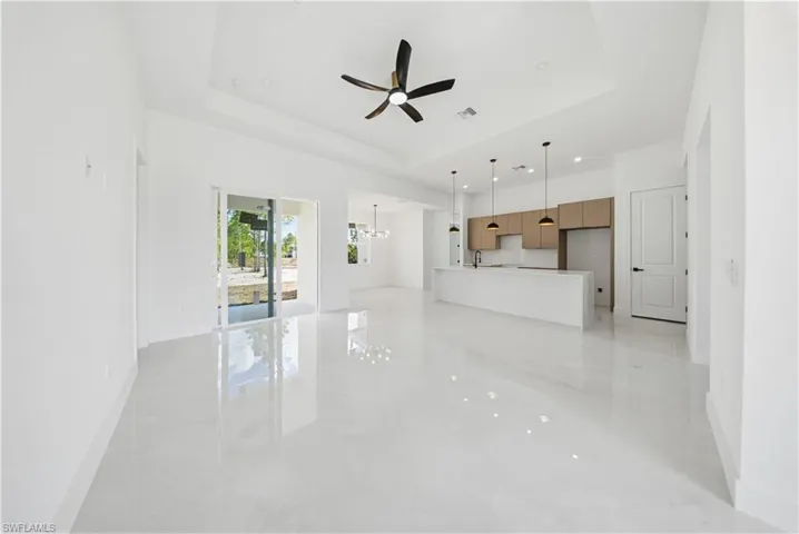 Unfurnished living room with ceiling fan, a tray ceiling, and a chandelier